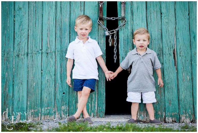 two little boys holding hands stand in front of rustic green barn door