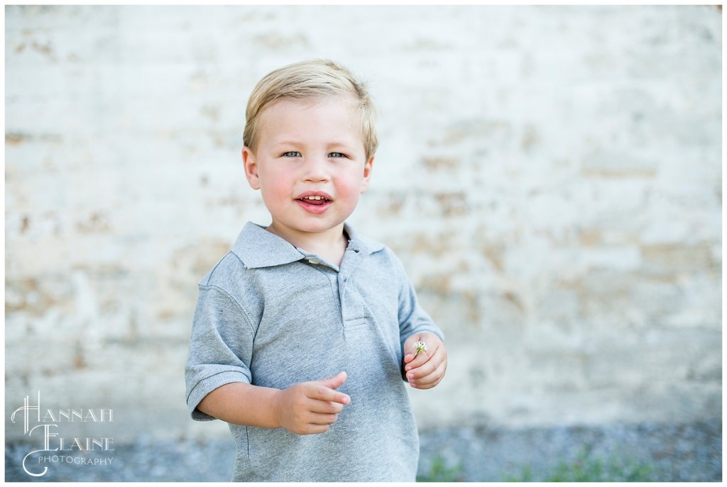 blond boy holds a flower in front of crumbling brick wall