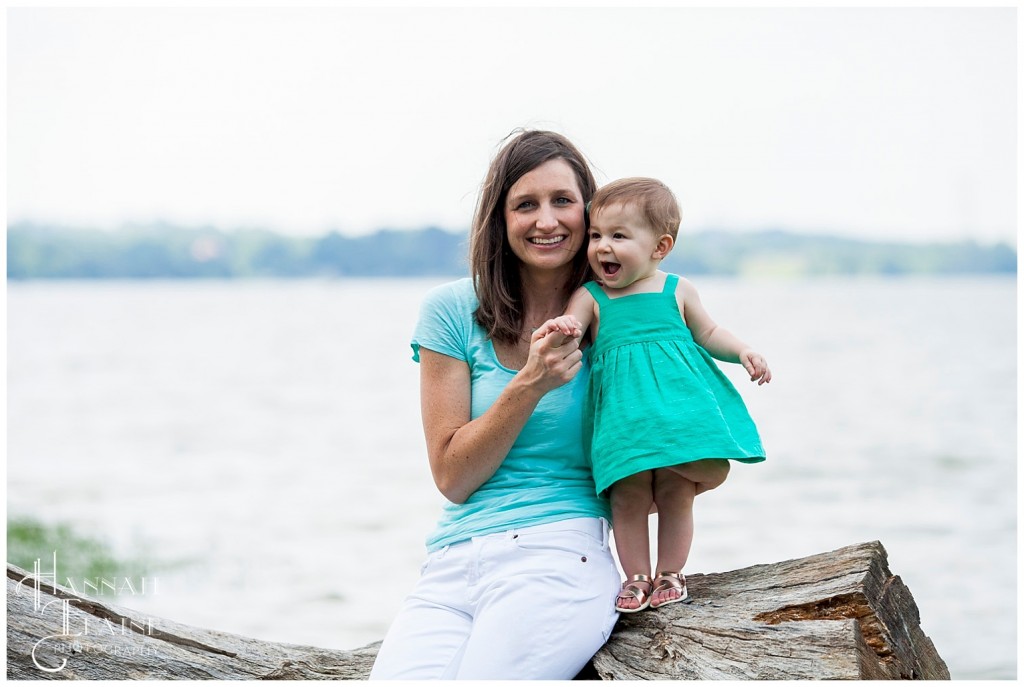 mom helps her daughter stand on drift wood by the water