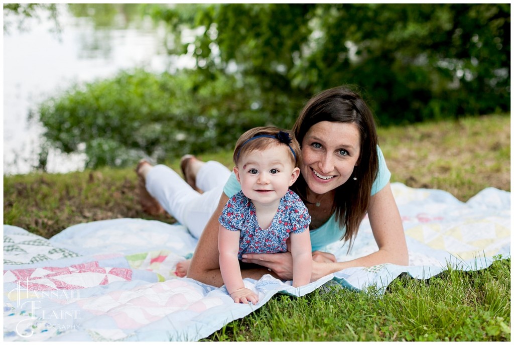 mom and daughter cuddle on a blanket at the park by the lake