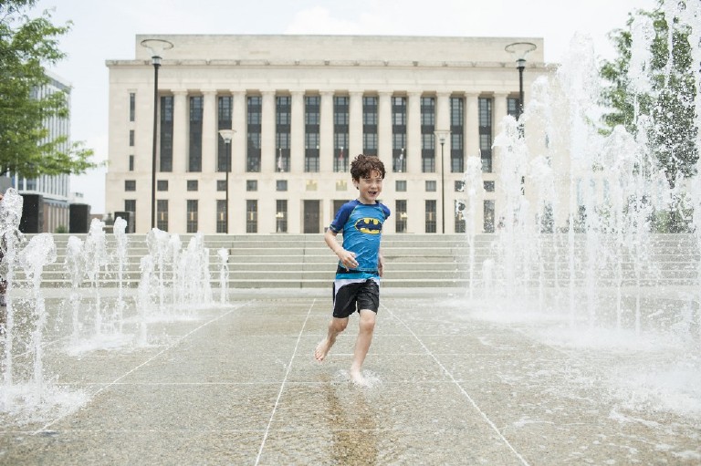boy in batman swimwear runs through fountains