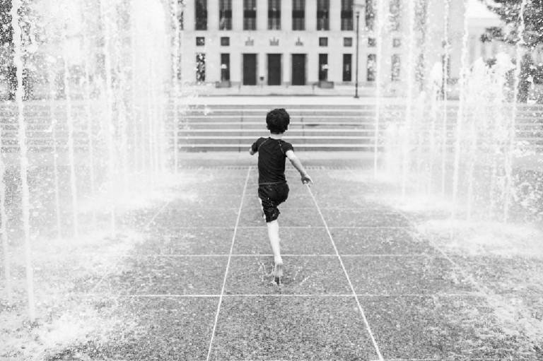 black and white image of boy running through the fountains