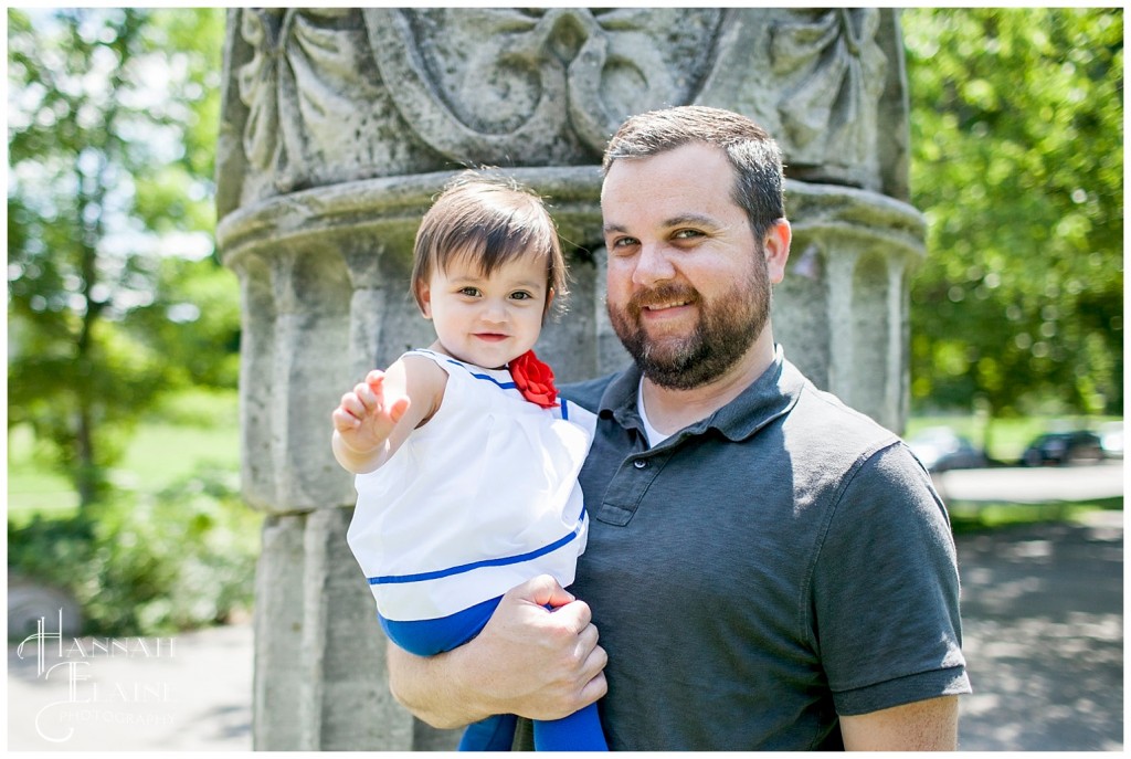 dad holds his little girl in front of an ornate roman pillar