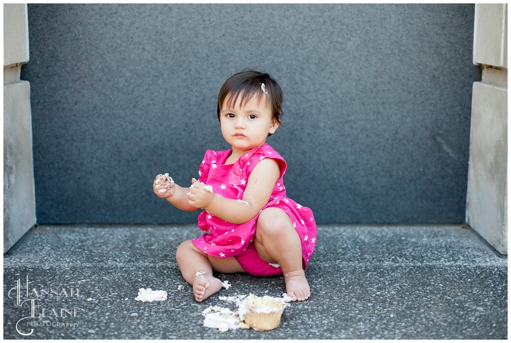 girl in pink dress tastes her birthday cake