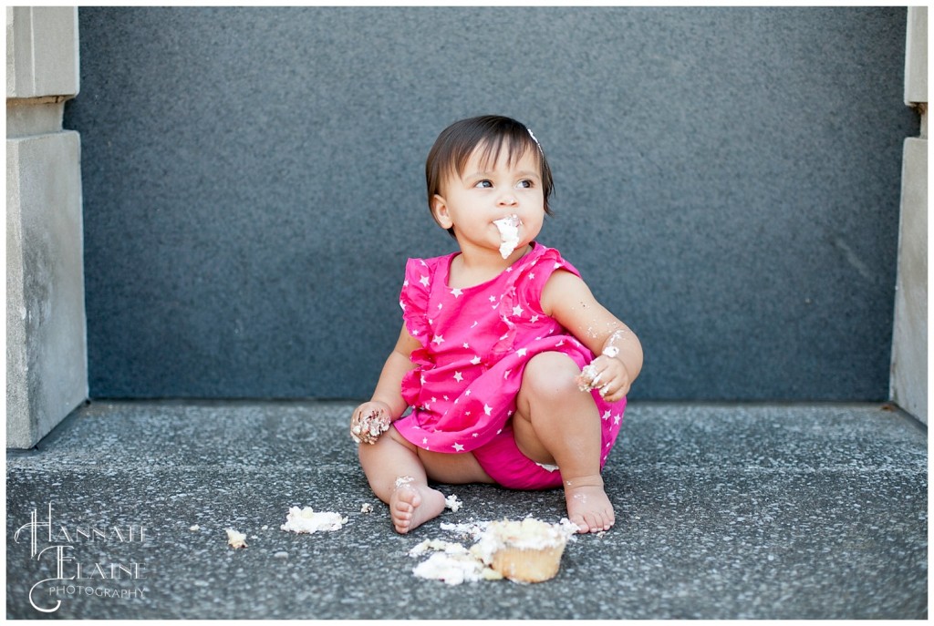 one year old in pink dress tastes her birthday cake