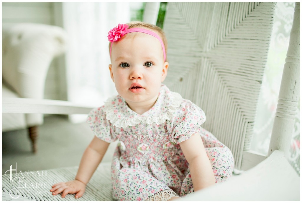 little girl with pink bow sits on white rocker