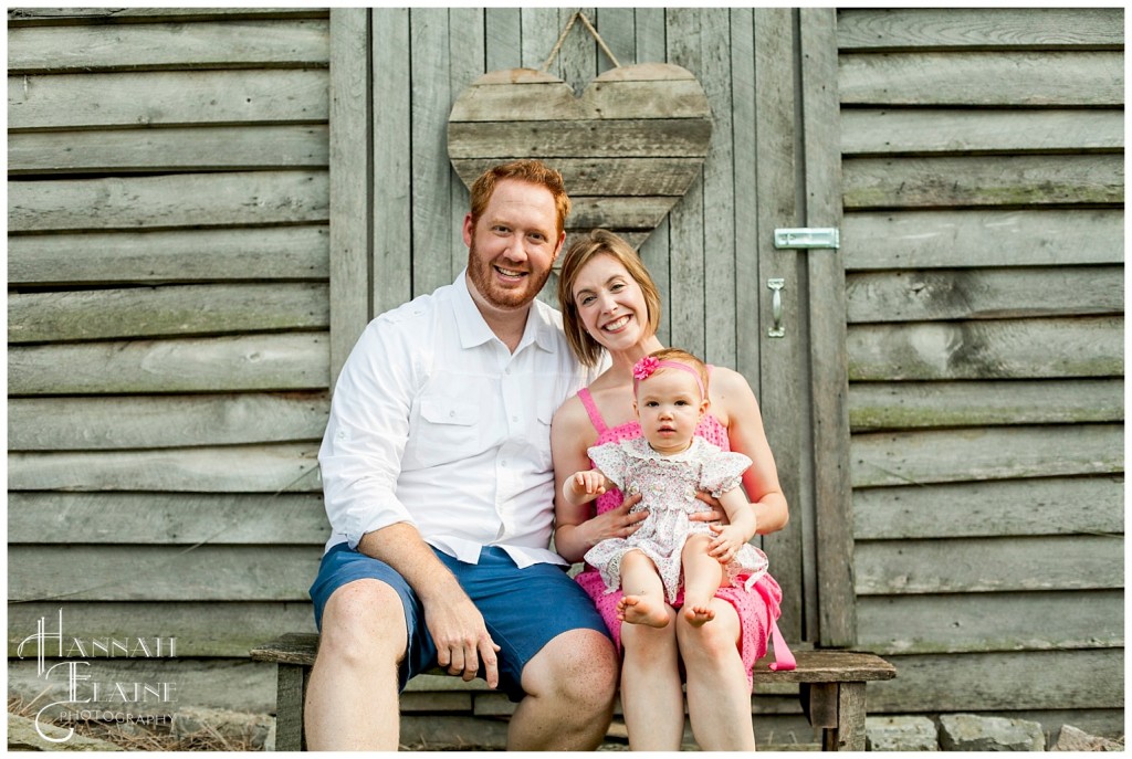 belle and her mom and dad in front of rustic barn