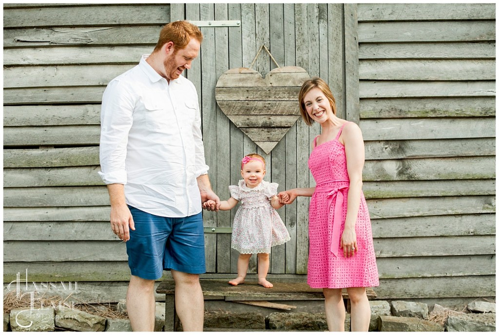 one year old girl learns to stand in front of rustic barn