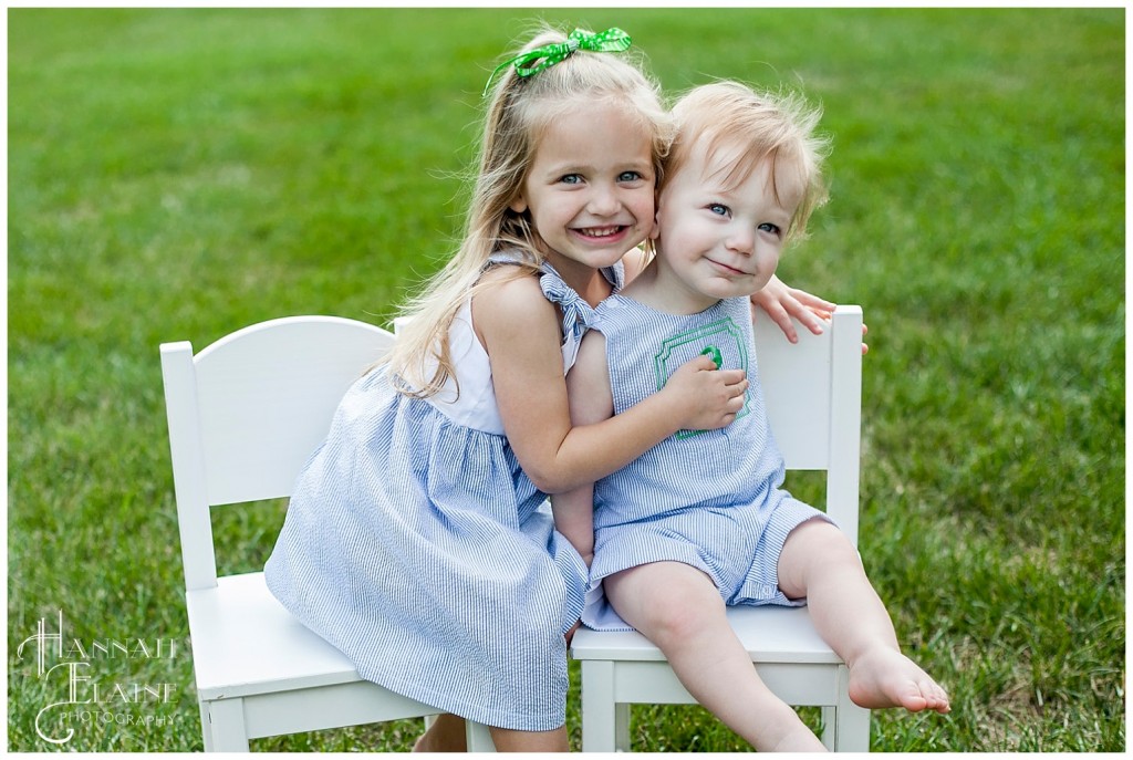 brother and sister in matching monogram outfits sit in white chairs