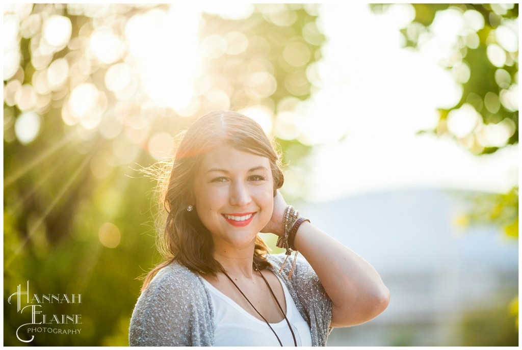 brunette stands in front of tree with sun bleeding through the leaves