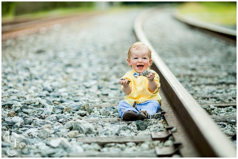 little boy in bow tie plays on the railroad tracks