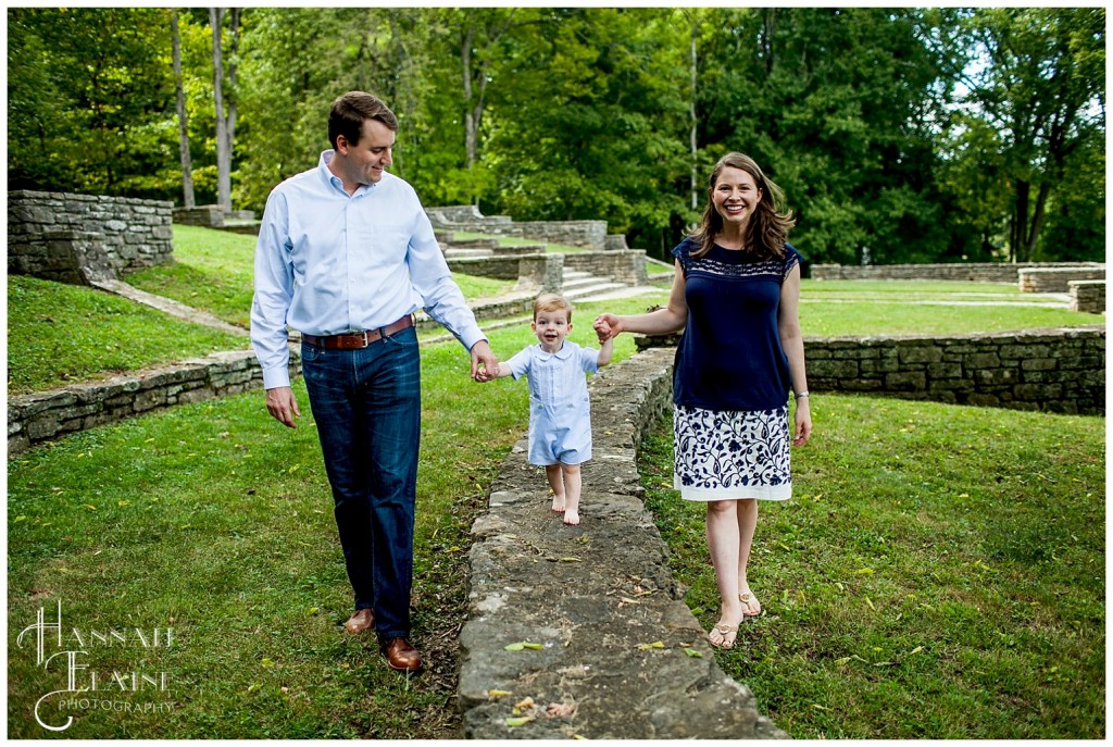 parents help their son walk along the top of an old rock wall border