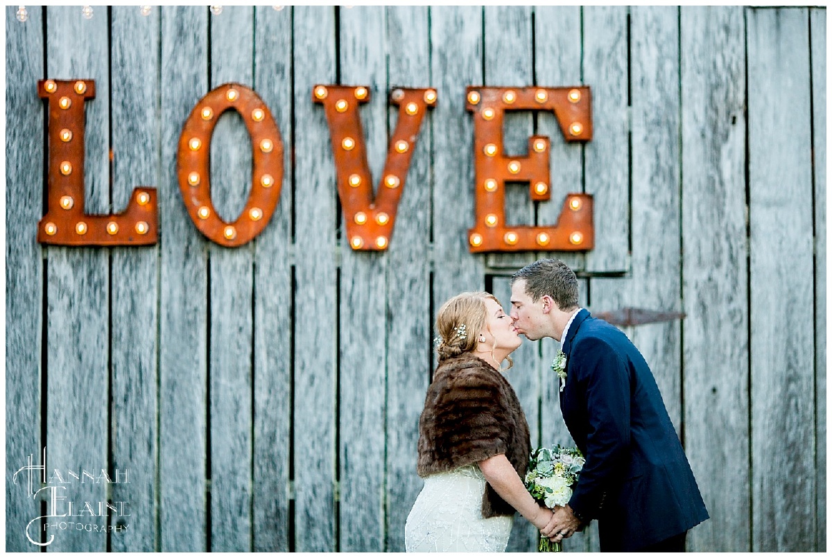 groom and bride in vintage fur in front of love marquee at drakewood farms