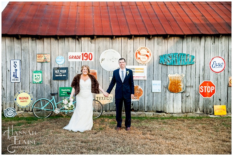 bride and groom in front of rustic barn with vintage metal signs 
