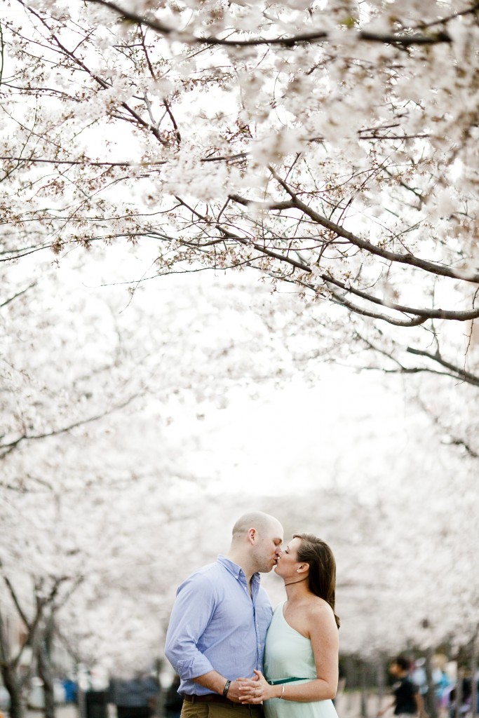 a couple kisses under the white blossoming trees on 1st avenue at the riverfront in downtown nashville