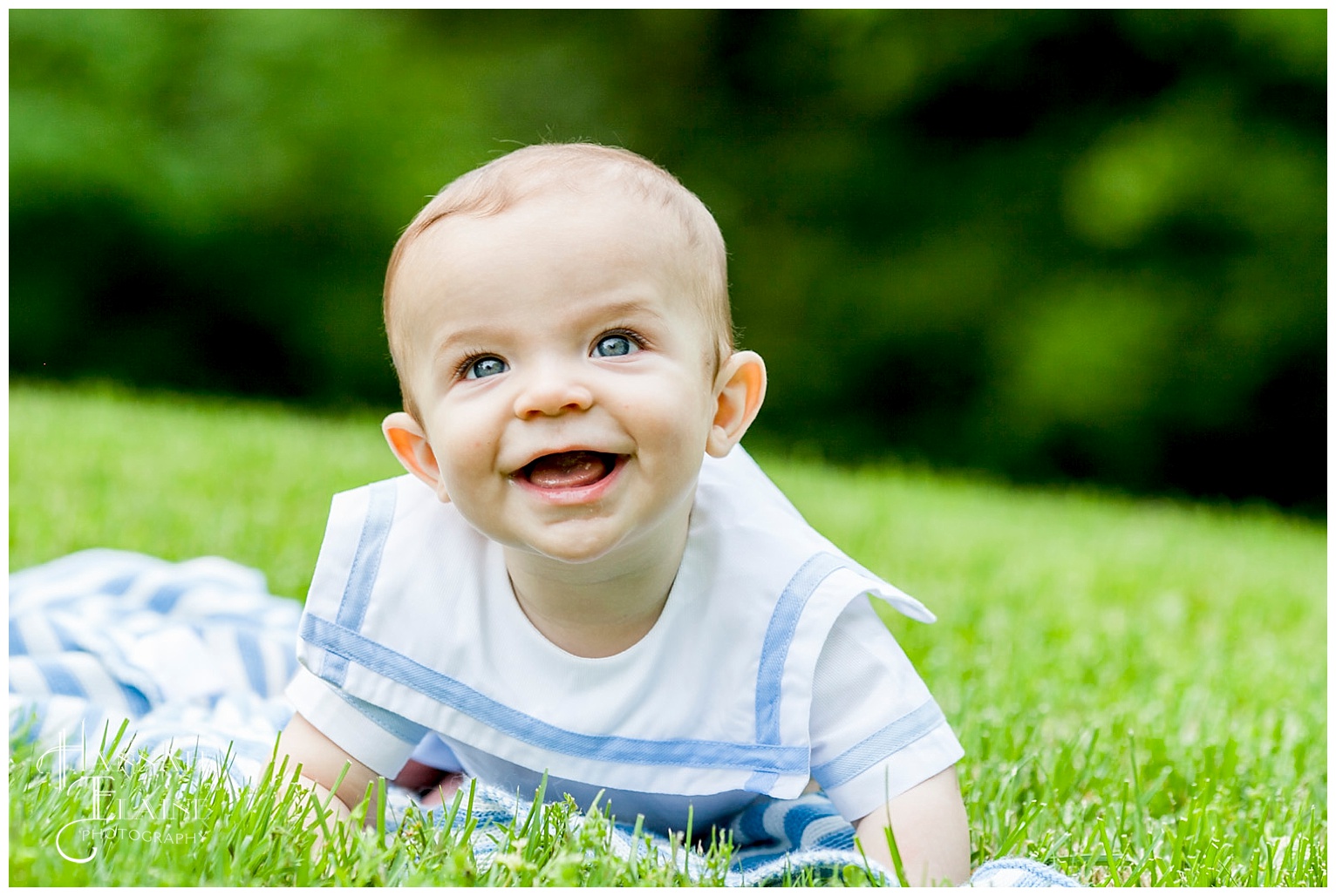 baby boy in blue and white frock smiles in the grass