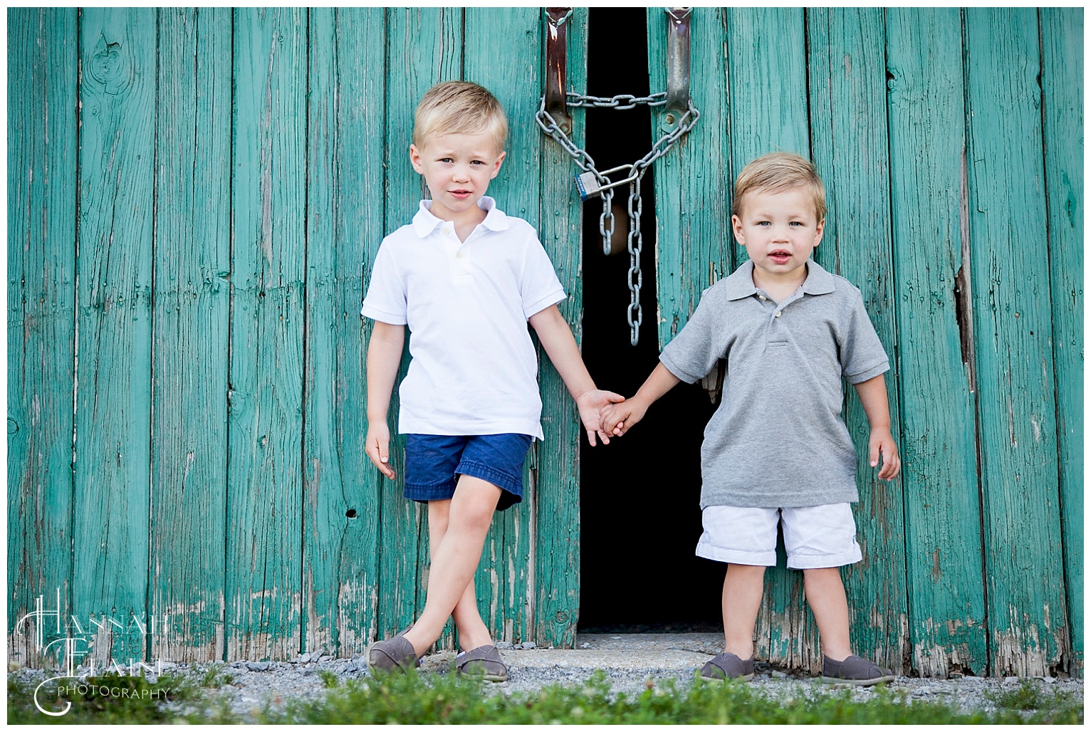 two little boys holding hands stand in front of rustic green barn door