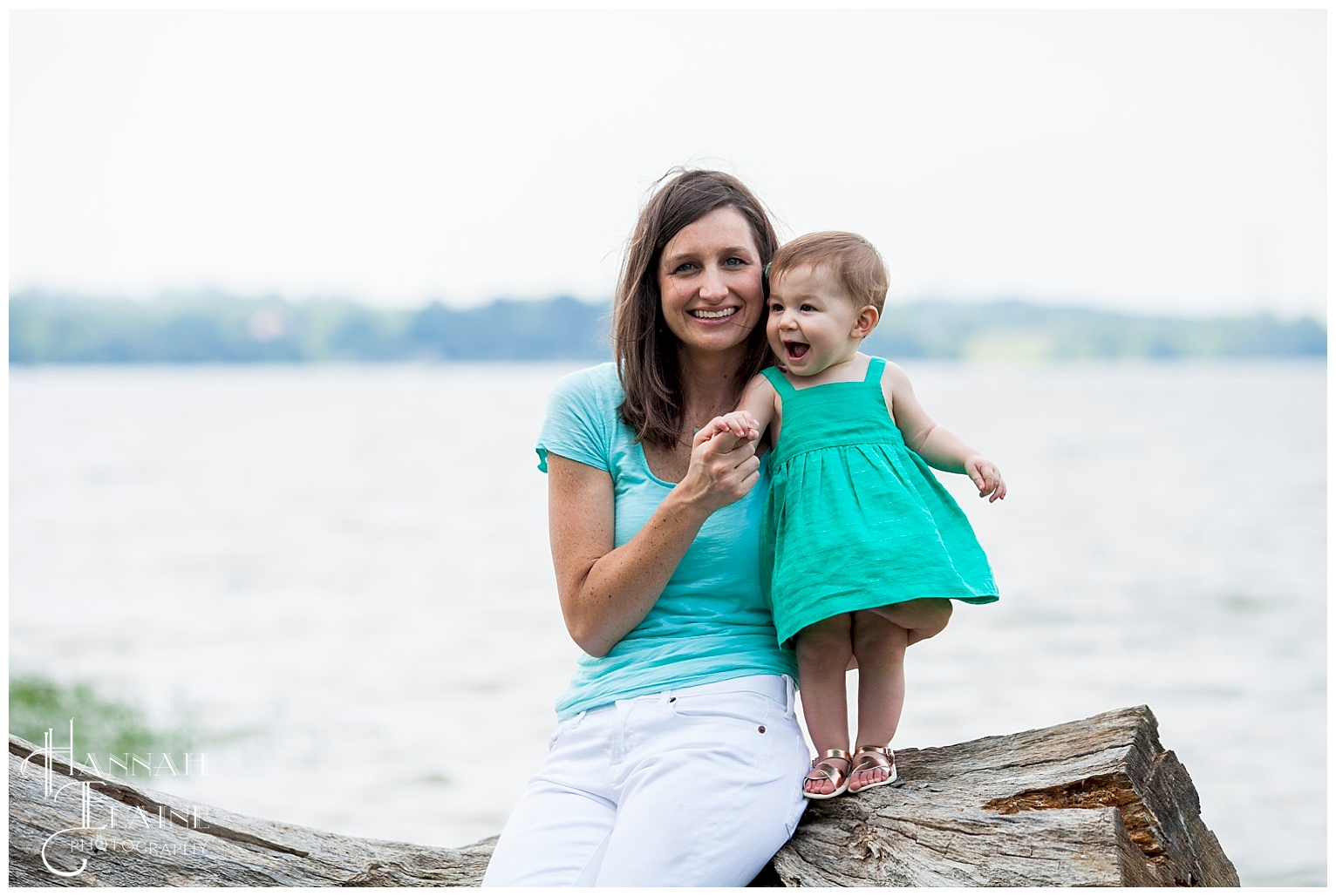 mom helps her daughter stand on drift wood by the water